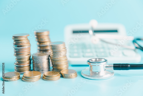 Fotografía Stacks of coins beside a stethoscope and calculator on blue background, illustra