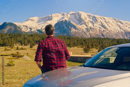 Foto A man in a red plaid shirt leaning against his car hood enjoying the view of sno