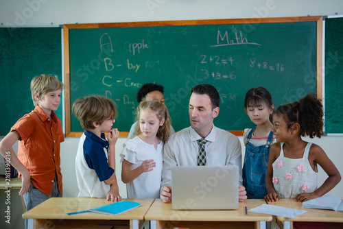 International school teacher and diverse elementary students gather around laptop for technology learning, digital education and collaborative classroom activity.