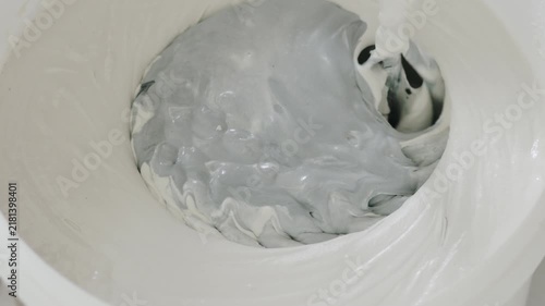 Slow motion closeup mixing black ink into decorative concrete plaster to make gray