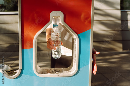 Obraz na plátně Person fills a plastic bottle with drinking water while walking in the city in summer