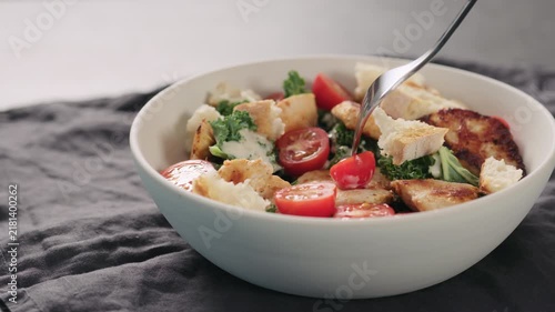 Slow motion man tastes caesar salad with kale and turkey in white bowl