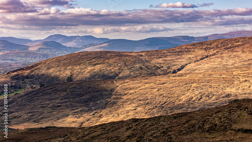 Fotografie A panoramic view captures rolling hills with dry, brown vegetation under a cloudy sky