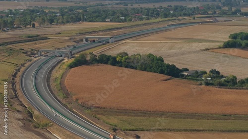Aerial view of the new A7 Autostrada Moldovei highway under construction near Bacau, crossing rural agricultural fields under clear daytime sunlight. 4K video.