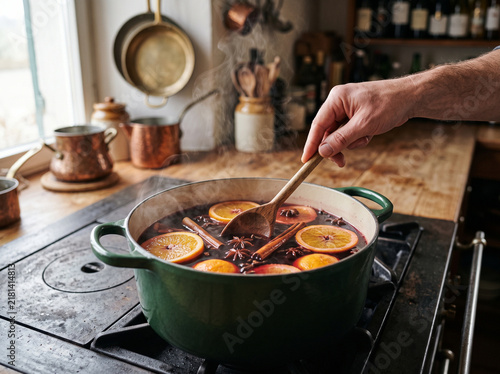 Cooking hot spiced mulled wine with sliced oranges, cinnamon sticks, and star anise in a pot on a stove