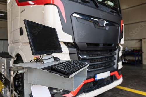 Truck service.  Computer diagnostic workstation in modern truck service garage station with heavy semi truck undergoing wheel alignment and technical maintenance checkup.
