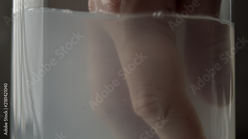 Foto Hand submerged in clear water inside a glass container, with curled fingers, visible skin texture and reflections