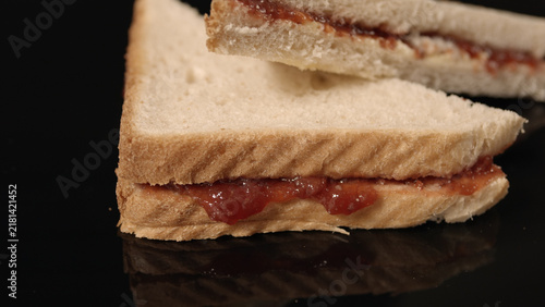 Two jam sandwiches stacked on a black reflective surface, showing red jam between white bread slices with visible crusts.