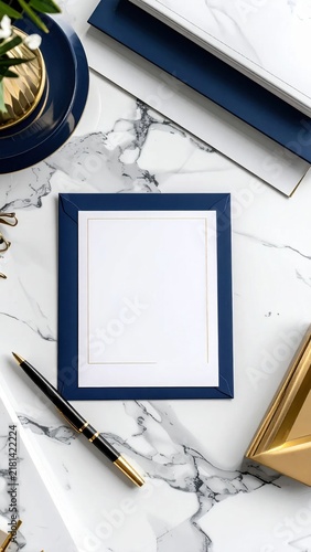 Top view of a blank blue invitation card with golden frame on marble desk with pen and accessories