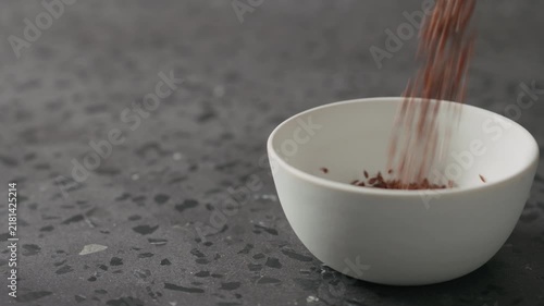 Slow motion flaxseed falling into white bowl on terrazzo countertop