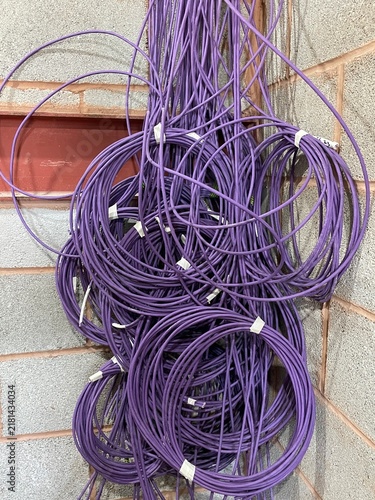 Bundle of purple network cables hanging on a brick wall, ready for installation