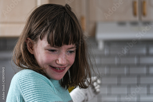 Картината върху платно Candid portrait of a smiling young girl with freckles and brown hair in a bright kitchen, looking down with a happy and natural expression