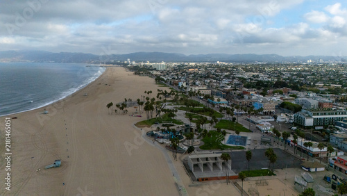 Aerial view of Venice Beach with its wide sandy shore, palm trees, recreational areas, and the urban cityscape of Los Angeles, California, United States.