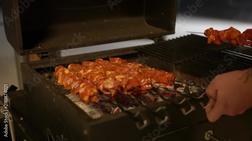 Closeup of a man hand places skewers with freshly marinated meat on a grill with burning coals to cook shashlik for an outdoor dinner.