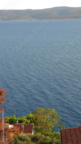Distant sailboat on calm blue sea beside coastal hillside homes
