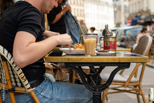 Obraz na plátně A man dines at an outdoor brasserie terrace in Paris, France, using a fork to eat potato gratin