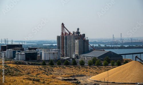 Umatilla, United States - 15 August 2026: Aerial view of McNary Elevator Dock with its large grain silos, storage tanks, and a massive pile of grain near the Columbia River.