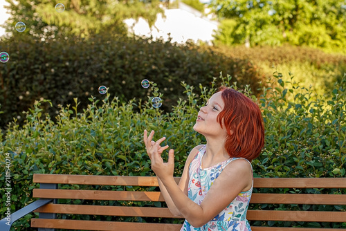 A portrait of a sweet girl playing with soap bubbles in a public park.