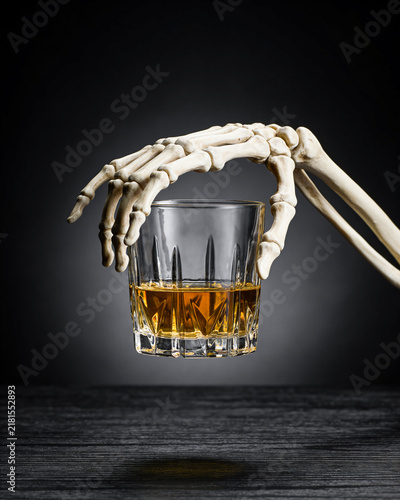 Halloween whiskey cocktail on black background. Skeleton is drinking alcohol at the counter. Alcoholic drink on dark stone table. Spooky, scary, fun, horror, creative. Bar holiday menu. Vertical