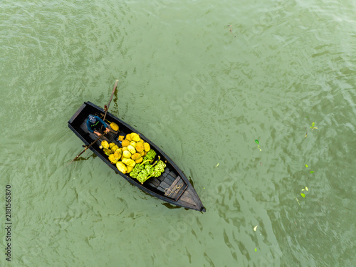 Rangamati, Chittagong Division, Bangladesh - 31 May 2025: Aerial view of a boatman rowing a wooden boat filled with jackfruits and bananas on the calm water.