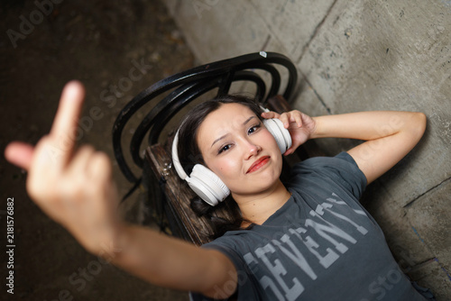 Young woman on a bench listens to music and shows her middle finger