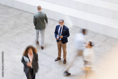 Focused businessman holds smartphone in modern office among crowd