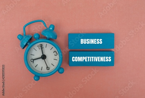 Bild auf Leinwand Blue alarm clock next to wooden blocks with BUSINESS COMPETITIVENESS text against coloured background