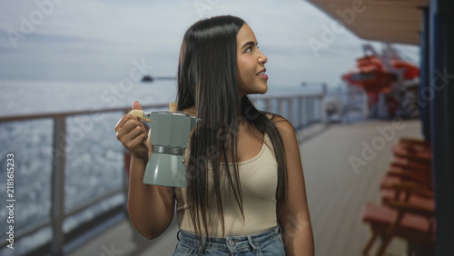 Foto Young hispanic woman smiling and holding a moka coffee pot on a cruise ship deck building, facing camera while offering the brew; morning calm