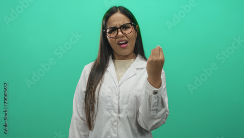 Photography Young hispanic woman doctor in white lab coat, hands raised in a questioning shrug gesture in a studio with green backdrop; confusion uncertainty