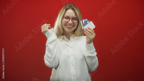 Quadro su tela Woman holds a bunch of creditcards in her right hand while covering her face with left palm and smiling toward camera in studio; financial joy