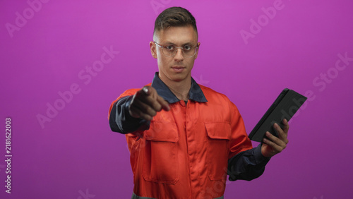 Foto Man mechanic in orange coverall holds tablet and beckons with hand in studio; confidence readiness skill