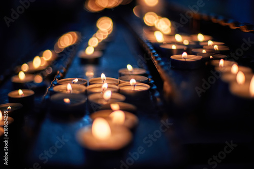 Quadro su tela Tealight candles create warm candlelight bokeh across a dark surface, suggesting meditation, remembrance, ceremony, spirituality and intimate evening ambiance