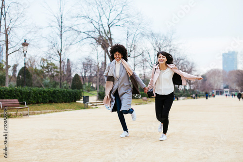 Spain, Barcelona, two exuberant women running in city park