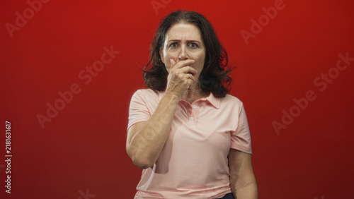 Bild auf Leinwand Woman covers mouth with hand in studio wearing pink shirt and ring, staring anxiously at camera; concern uncertainty