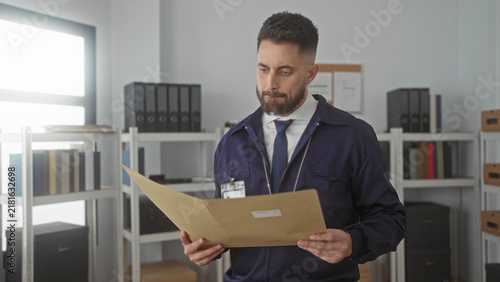 Hispanic man reading a folder in an office building, holding the file with both hands and an id badge visible; investigation focus.
