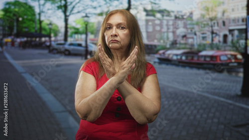 Foto Older hispanic woman with hands crossed in an x across her chest on a cobbled city street, face solemn and eyes closed showing refusal; defiance solitude