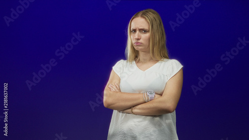 Foto Woman with crossed arms, furrowed brow and wristwatch wearing white blouse in studio blue backdrop; disapproval resolve