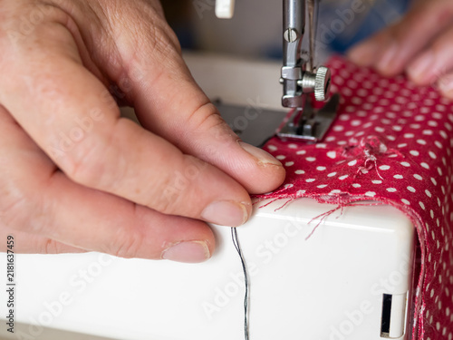 Close-Up of Hands Guiding Red Fabric Through Sewing Machine