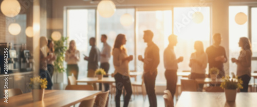 A group of people socializing in a bright room with warm sunlight filtering through large windows. The atmosphere is lively and engaging, ideal for gatherings.