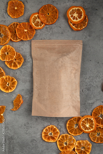 Empty brown kraft paper packaging bag and scattered dried orange wheels on a gray concrete background top view
