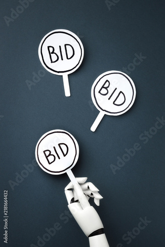 Obraz na plátne A white robotic hand holding bidding paddle with BID signs among two others on a a dark gray background