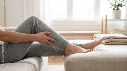 Person massaging sore calf muscle while resting on a comfortable sofa at home