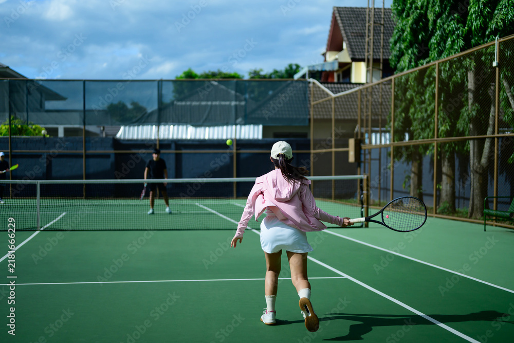 Obraz premium Young Asian Woman Playing Tennis on Outdoor Green Court with Friends on a Sunny Day
