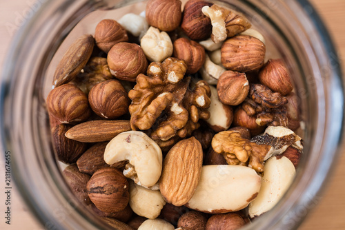 Close-up top view of glass jar filled with almonds, walnuts, cashews and hazelnuts on wooden table.