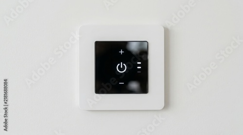 Control panel featuring a glossy dark touchscreen interface surrounded by a matte white square frame mounted on a neutral painted wall surface.