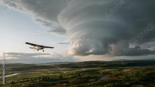 Small airplane flying over farmland under dramatic storm clouds during daytime