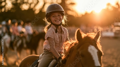 Smiling young girl wearing helmet riding brown horse during golden hour outdoor equestrian activity with blurred background people and trees