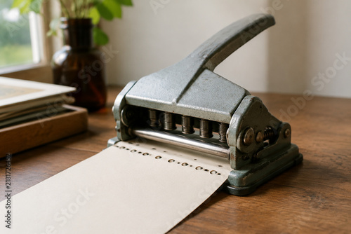Vintage manual paper perforator on a wooden desk, revealing a neat row of circular holes.