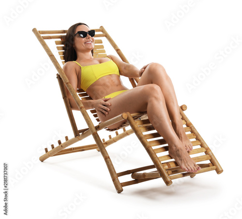 Foto Smiling tanned woman in sunglasses and swimsuit sunbathing on deck chair against