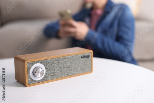 Modern audio speaker on white table and woman with mobile phone in room, selective focus